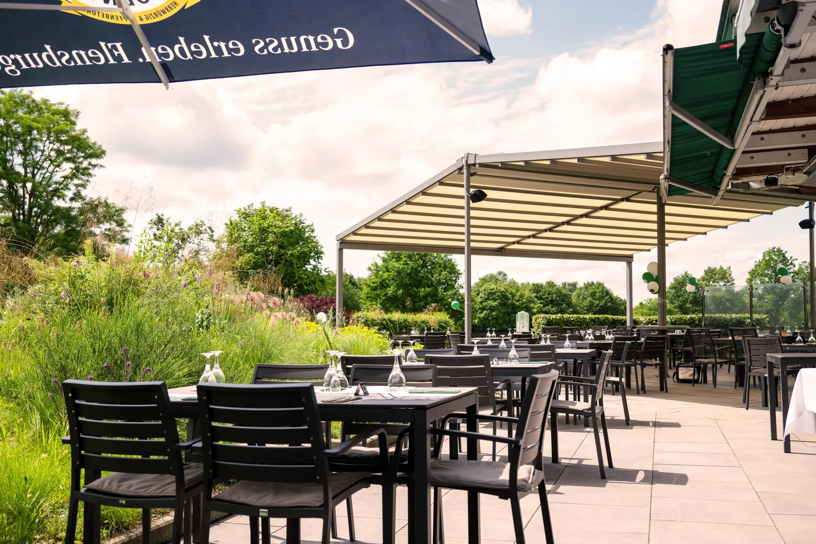 Sonnige Terrasse mit gedeckten Tischen und Blick in den Staudengarten